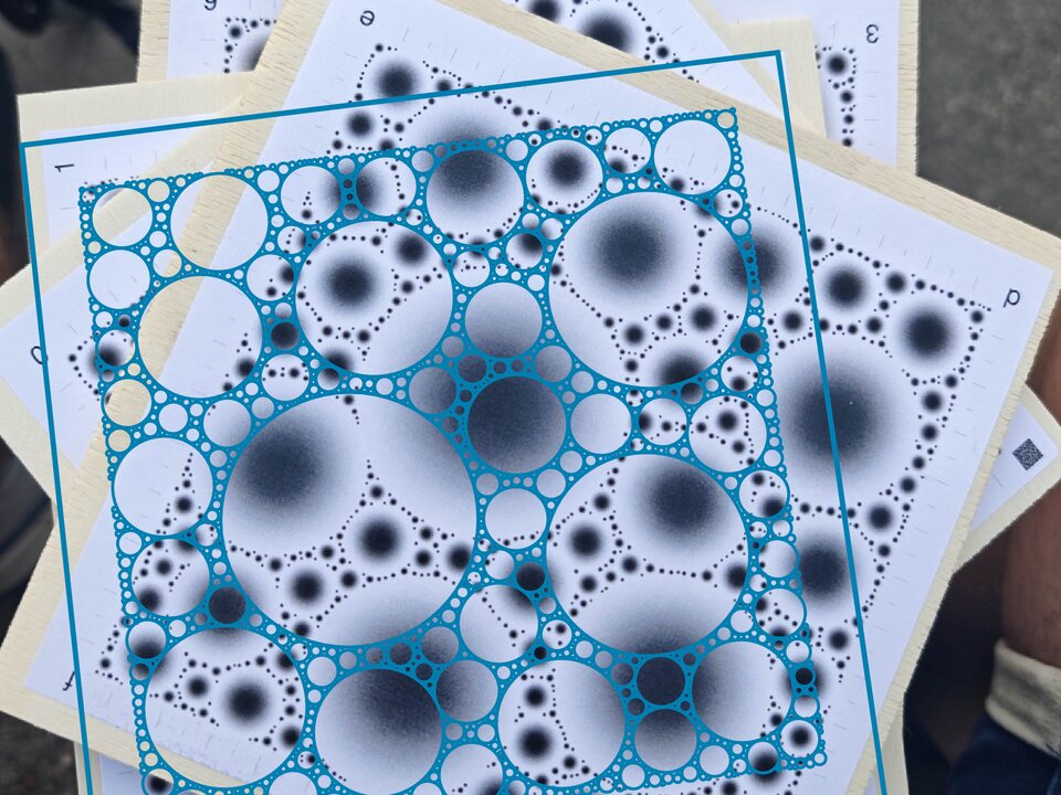 A stack of printed boards photographed obliquely; the top board has every blob outlined in teal with its fitted ellipse.